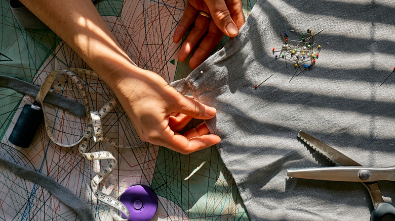 Person with sewing supplies pinning gray fabric.