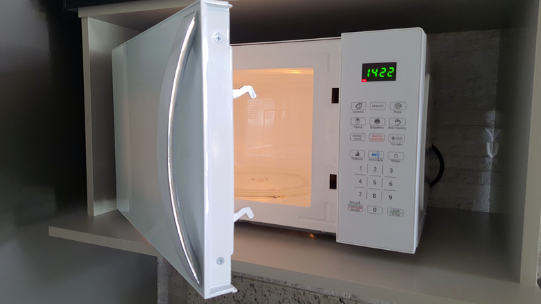 A white microwave with open door sitting on a cabinet shelf