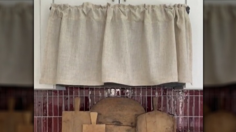 A simple curtain covering a microwave with cutting boards underneath