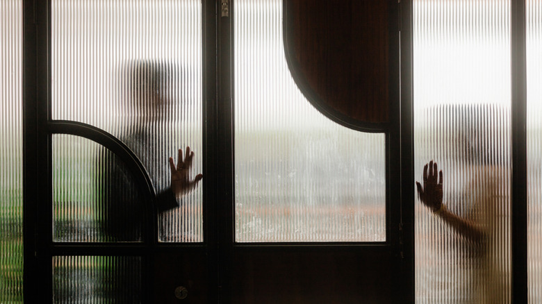 Figures silhouetted behind reeded glass with hands pressed against the surface.