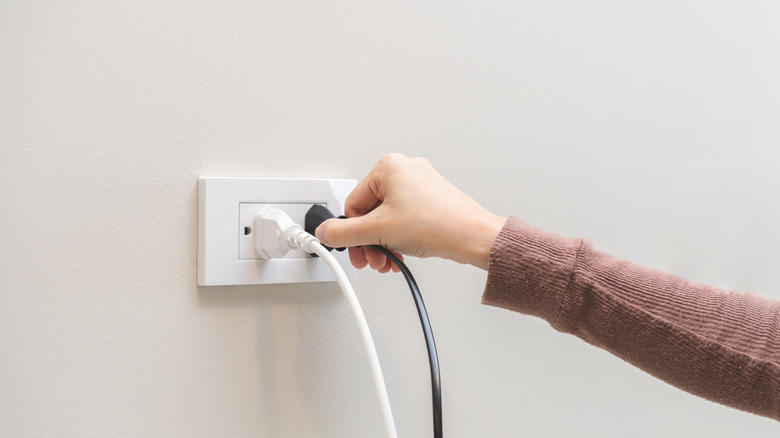 A hand plugging a cord into an outlet against a white wall
