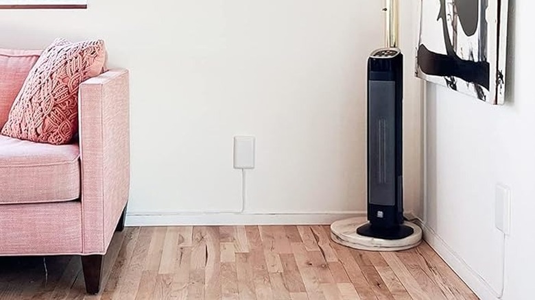 The Sleek Socket against a white wall between a fan and a pink couch in a living room