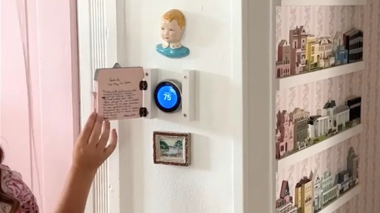Person opening cute pink cottage cover concealing thermostat