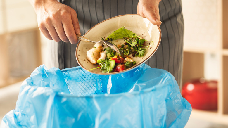 Man dumping plate of food into kitchen trash can