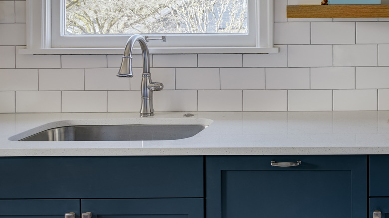 A kitchen sink features a full suite of cabinets underneath, including a false plate in front of the basin.