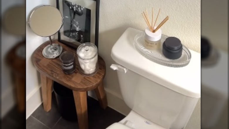 A stool covered in decorative items covers a trash can next to a toilet
