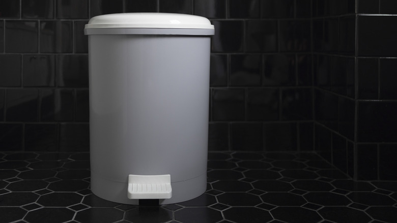 Trash can with lid in black tiled bathroom