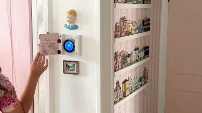 Person opening cute pink cottage cover concealing thermostat