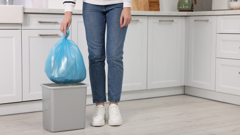 A person bags up trash from a trash can in the middle of the kitchen.