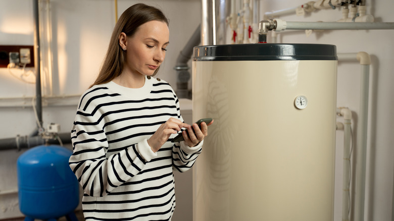 A concerned person stands near their HVAC system while on their cell phone