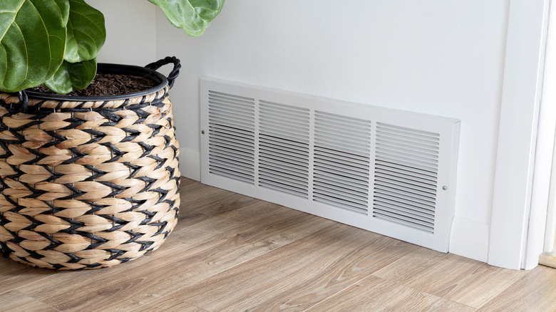Potted plant placed near a floor air return vent built into a white wall of a home