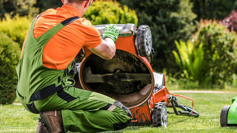 A lawn care technician kneels and checks a lawn mower in a garden during the day.