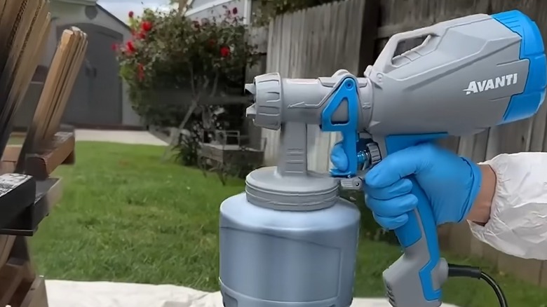 Hand holding Avanti's Handheld HVLP Paint and Stain Sprayer to spray deck chair outdoors