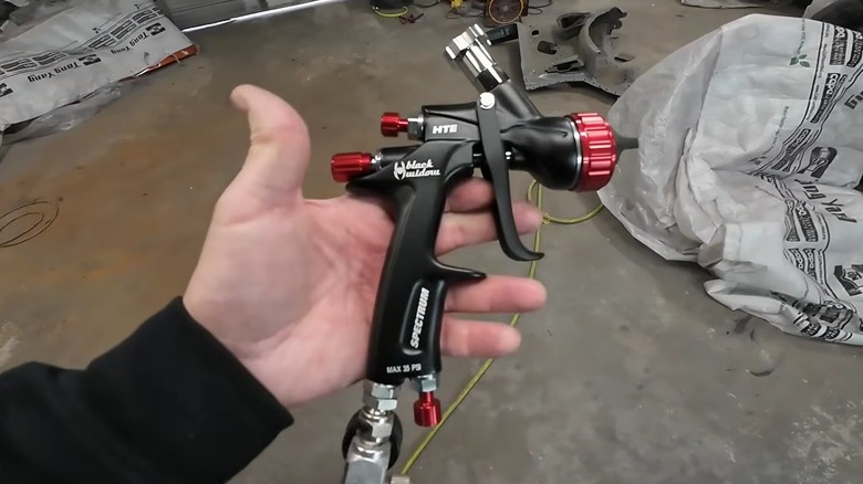 Hand holding Black Widow by Spectrum's Professional HTE Gravity-Feed Air Spray Gun with Rear Fan Control in garage work space