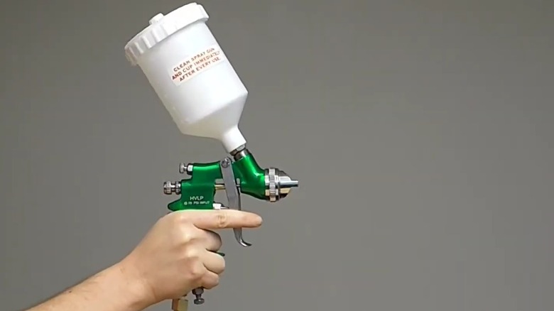 Hand holding Central Pneumatic's 20 ounce HVLP Gravity-Feed Spray Gun on gray background