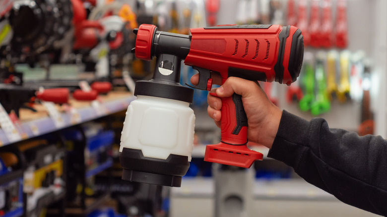 A man holding a cordless paint sprayer in a hardware store