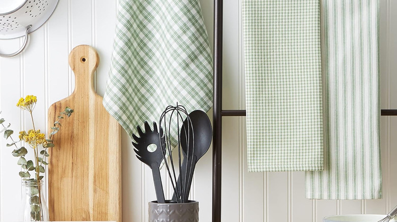 Pale green and white tea towels hanging in cozy kitchen beside cutting board and utensils