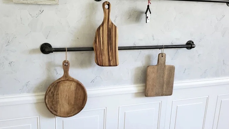 Wooden rustic cutting boards hung on black rod on wall as kitchen decor