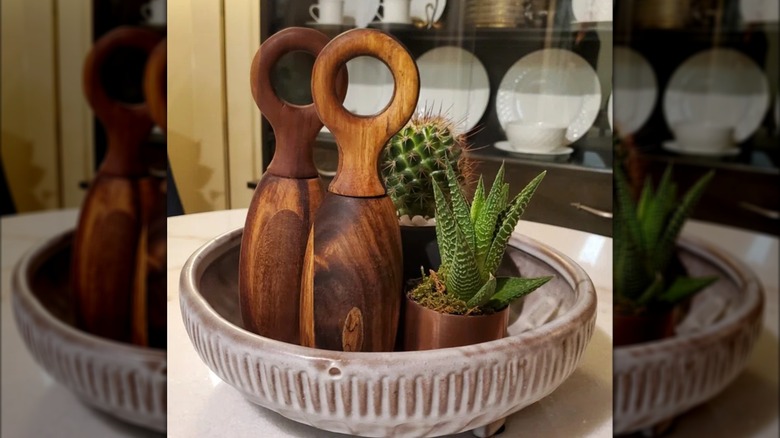 Wooden salt and pepper grinders in antique bowl with planted succulents