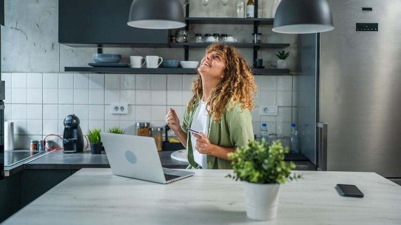 Excited woman using credit card on laptop in stylish modern kitchen