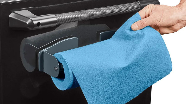 A hand pulls a paper towel from a magnetic paper towel holder.
