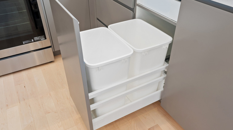 Two white trash cans in a silver cabinet