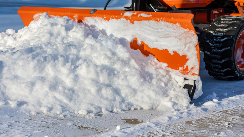 An orange plow removes snow from a driveway