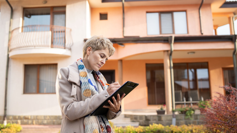 A person making notes on a clipboard outside of a home
