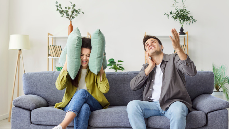 Couple sits on the sofa at home living room, covering ears due to loud noise