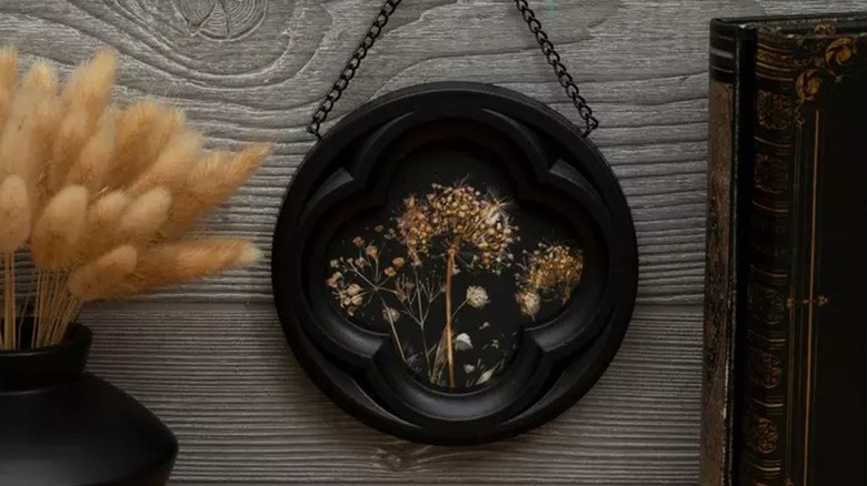 A decor piece with a black frame and a dandelion  suspended in black resin, hanging on the wall.