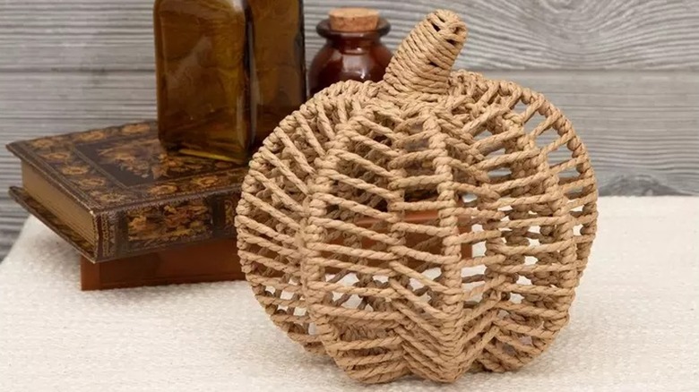 A woven wicker pumpkin placed in front of decorative books on a tabletop.