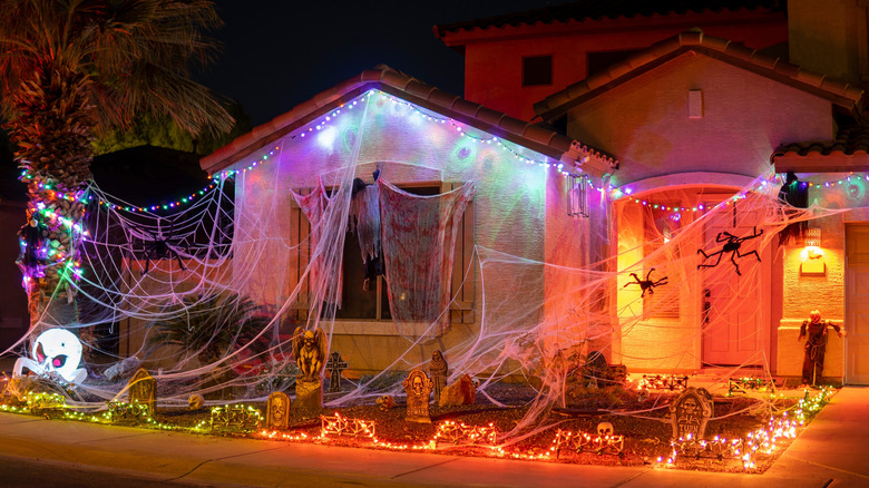 Home decorated for Halloween with large woven cobwebs, fake spiders, graveyard stones, and orange lighting effects