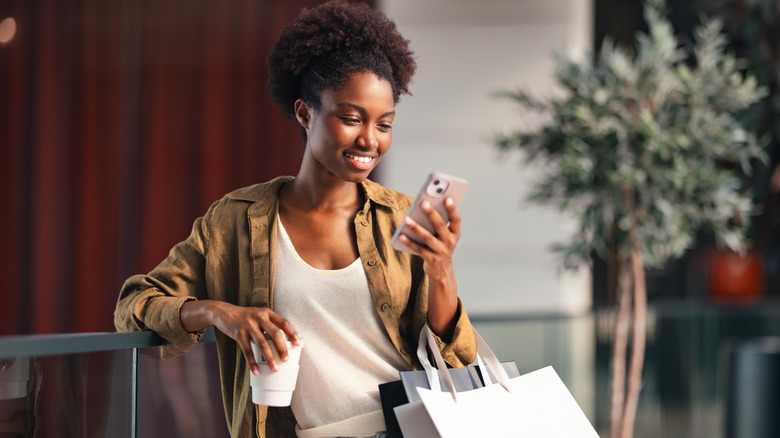 woman shopping on her phone with bags on her arms