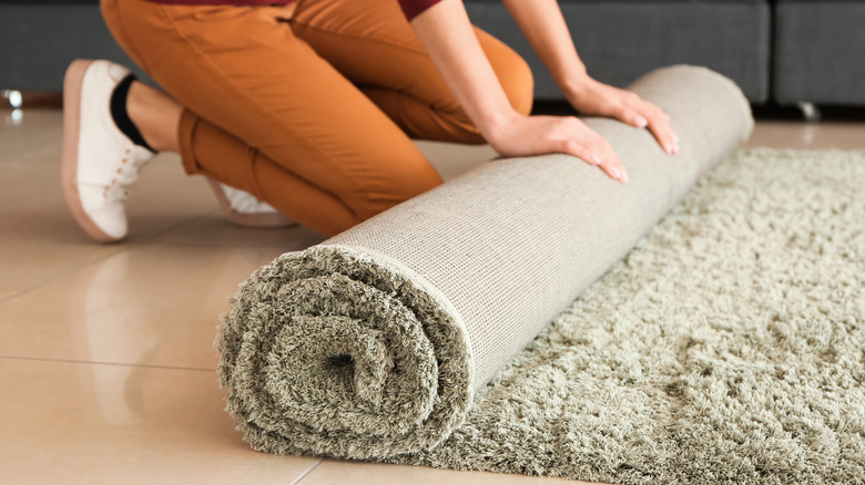 A person unrolling new rug onto a tile floor
