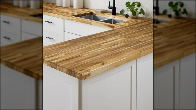 A Hampton Bay butcher block sits as the countertop on white cabinets and drawers in a kitchen.
