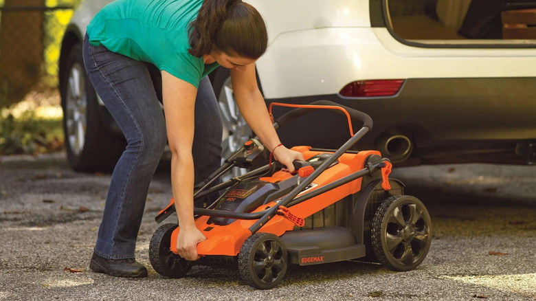 a woman folding a Black and Decker lawn mower to fit in the back of her car