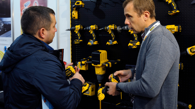 Two men shopping for DeWalt power tools near a wall of drills on display.