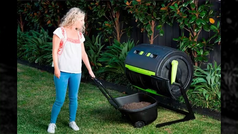 A woman with curly blond hair pulls a cart of compost from a compost tumbler.