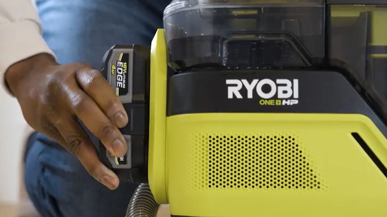 A dark-skinned hand attaches a battery to a Ryobi tool.