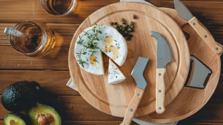 A split level cheese board with tools and a wheel of brie on top