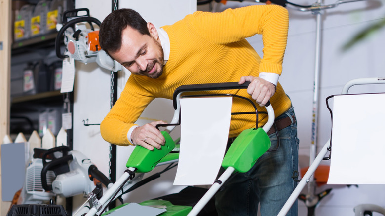 A man in a yellow sweater looking closely at a lawn mower for sale