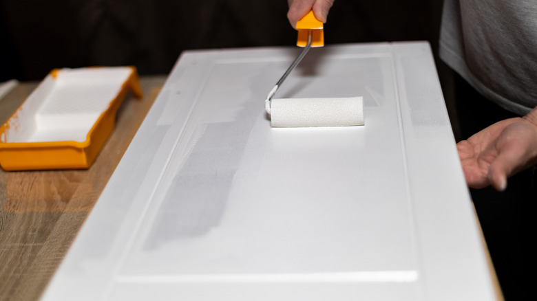 A person painting the door of a cabinet.