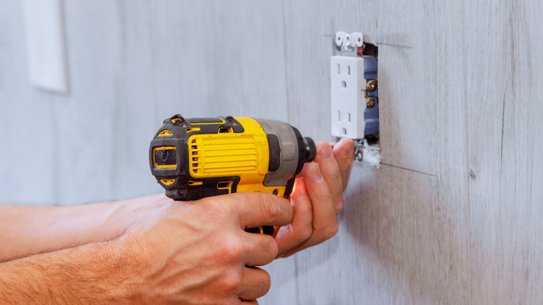 electrician installs an outlet using screwdriver