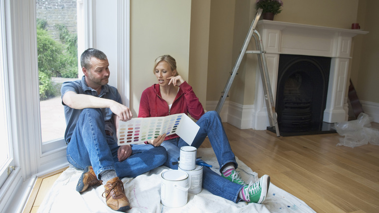 Couple looking at paint samples sitting on a dust sheet surrounded by paint cans and a step ladder
