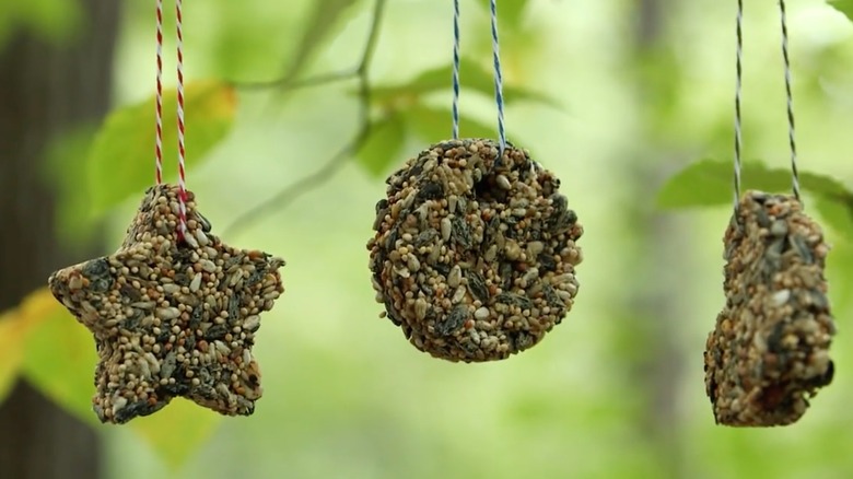 Three shaped ornaments hang from a tree by string.