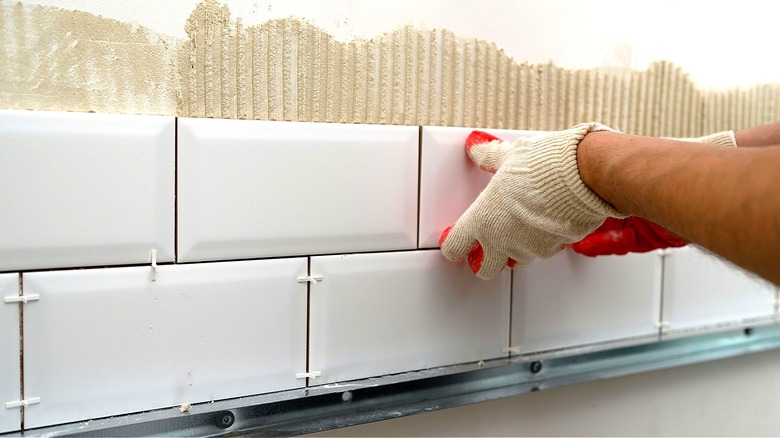 Close-up of a person applying plain white tiles to a wall