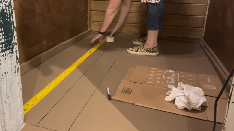 A person lays out a tape measure to draw Sharpie lines on a brown floor