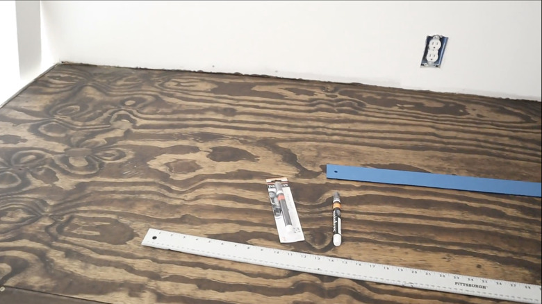 A stained plywood floor with measuring sticks and paint pens on it