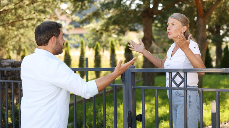 A male and a female neighbor argue about a fence dividing their properties.