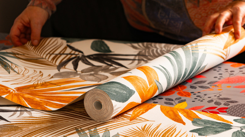 A pair of hands unrolls a section of bold, floral wallpaper.
